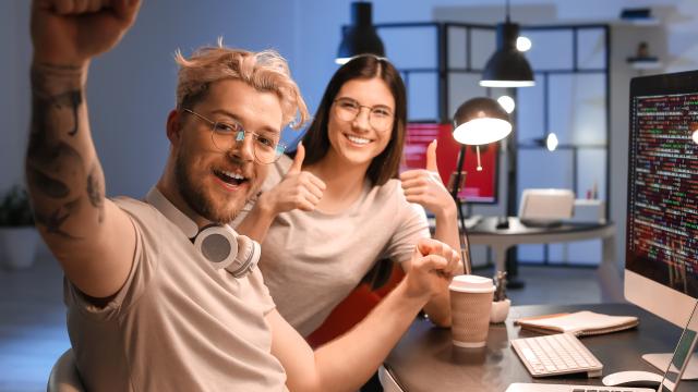 Two students sitting next to each other cheerful with the work they are doing on the computer