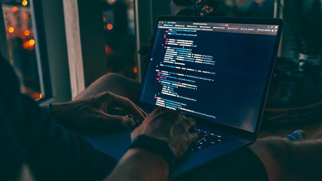 Image of hands typing with computer screen that has coding language on it.