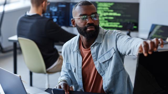 Person working on a computer screen with coding text on screen behind them