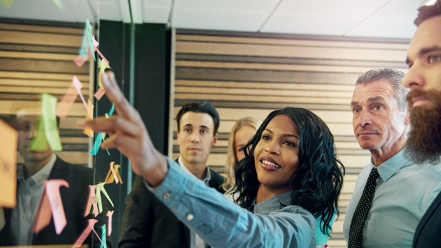 Group leader as working picking up post it note on board while staff are behind